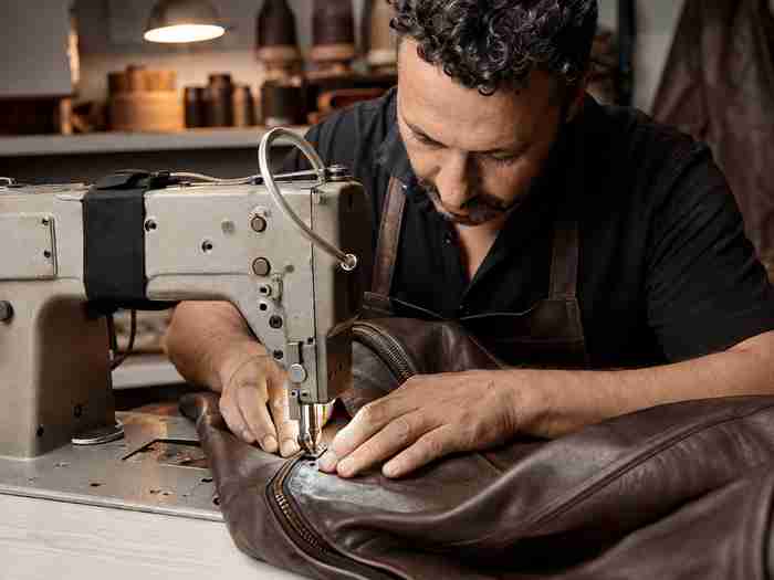 craftsman stitching a custom leather jacket on an industrial sewing machine